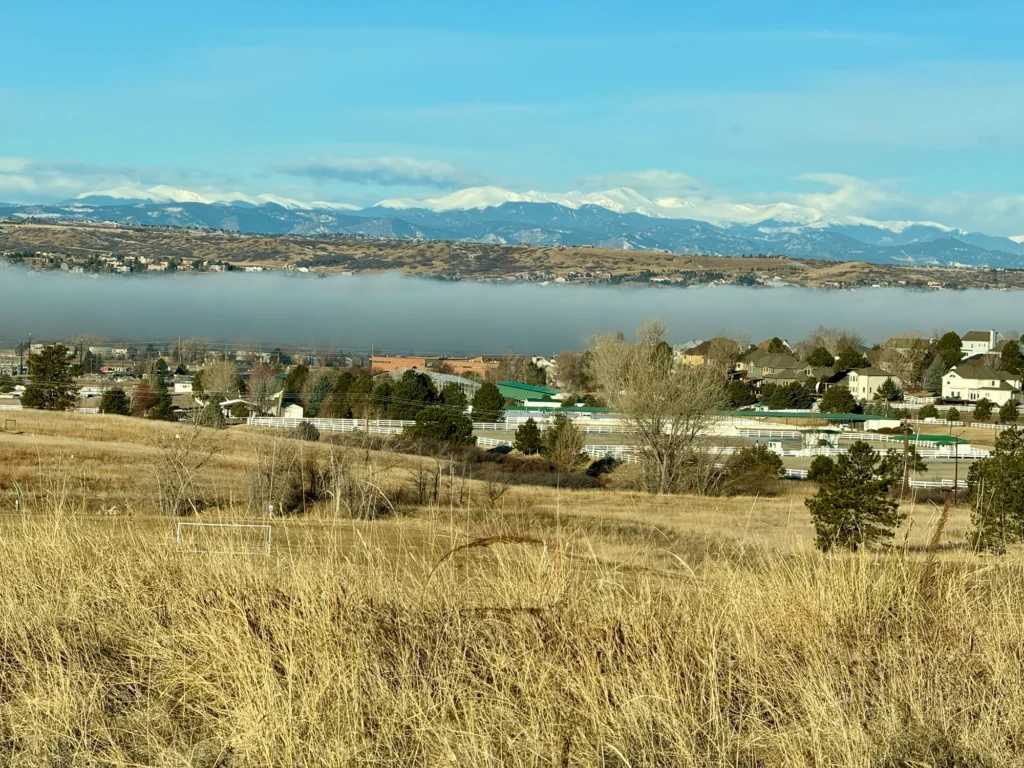 A low layer of fog settles in over the Denver suburb of Parker, Colorado. Neighborhoods, a school, an equestrian facility and sport fields are in the foreground.